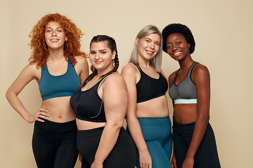 Different Race. Diversity Figure And Size Women Portrait. Smiling Multiethnic Female In Sportswear Posing On Beige Background. Body Positive As Lifestyle.