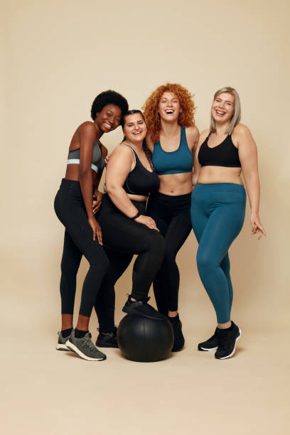 Diversity Models. Different Race And Size Women. Group Of Multicultural Friends In Sportswear With Black Fitness Ball On Beige Background. Sport For Active Lifestyle. Diversity Models. Different Race And Size Women. Group Of Multicultural Friends In Sportswear With Black Fitness Ball On Beige Background. Sport For Active Lifestyle. fitness ball photos stock pictures, royalty-free photos & images