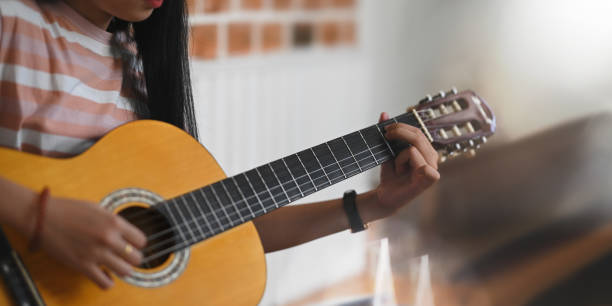 istock Cropped image of young asian woman practicing her skill on acoustic guitar while sitting over sitting room white wall as background. Woman with performing an acoustic guitar concept. 1225598376
