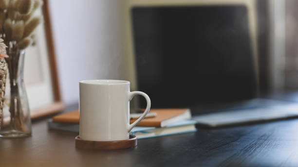 istock Coffee cup putting on black working desk that surrounded by stack of notebook, wild grass in vase, empty picture frame and computer laptop. 1225598537