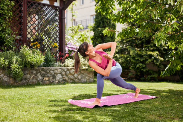 istock Young attractive brunette standing on the mat in her backyard in practicing yoga. Revolved Crescent Lunge yoga pose. 1225601989