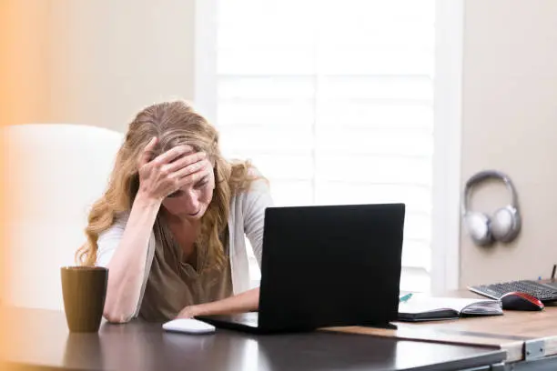 A mid adult businesswoman has her head in her hands during a stressful situation. She is looking at something on her laptop.
