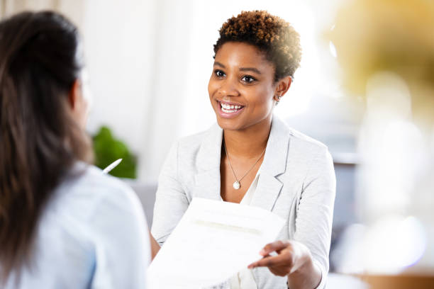 istock Attractive female counselor smiles while giving unrecognizable woman intake paperwork 1225603807
