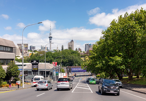 Auckland, New Zealand - Cars on a street in Parnell, Auckland, with the Sky Tower and the city's skyline on the horizon.