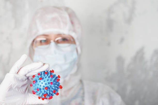 istock woman in protective suit holds coronovirus model 1225609220