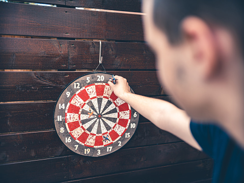 Teenage boy enjoying his hobby: He is outdoors on the patio, practising darts.