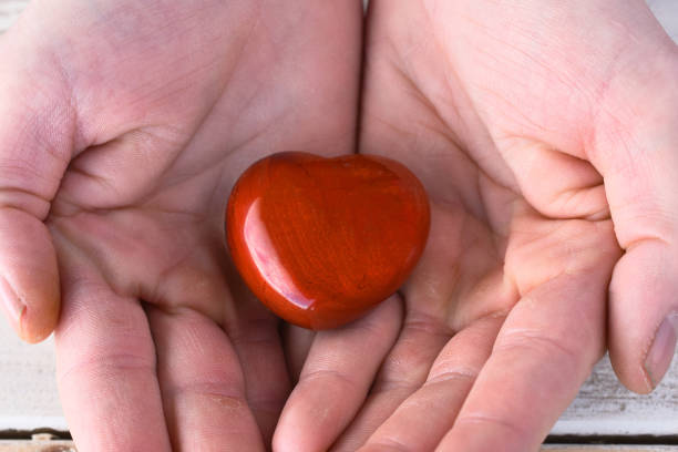 A close up image of a hand holding a heart shaped red jasper healing crystal.