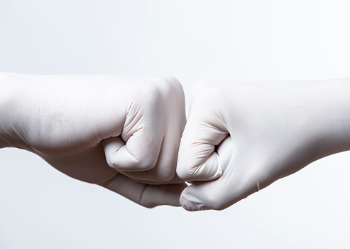 Two unrecognizable peoples fits wearing white protective gloves are touching each other in front of white background.
