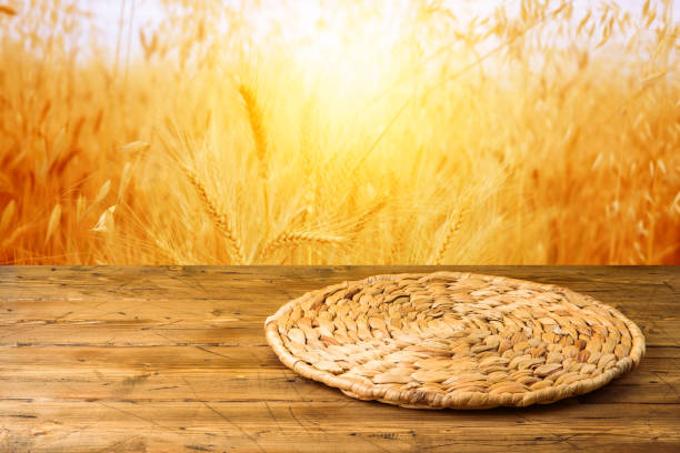 istock Empty wooden table with wicker round placemat over wheat field background. Harvest mock up background 1225614539