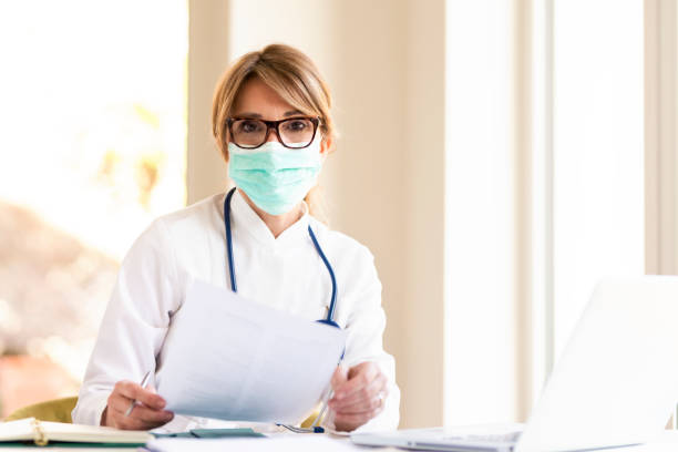 istock Female doctor wearing face mask while working on laptop in doctor's office 1225616305