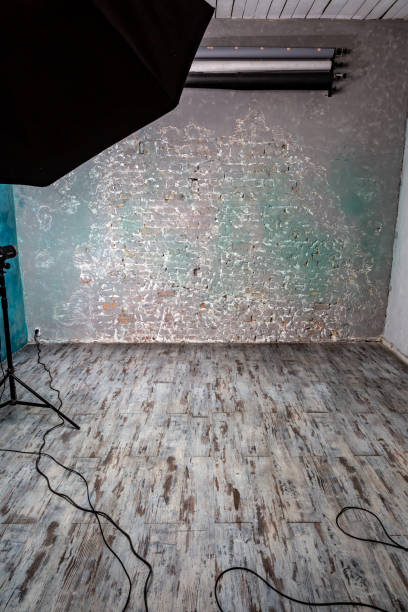 istock Empty photo studio with shabby wooden floor, brick wall, backdrops, light. Brown gray tones. Vertical orientation 1225619044