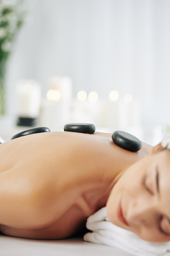 Close-up image of young woman lying on bed in spa salon with hot basalt stones along her spine