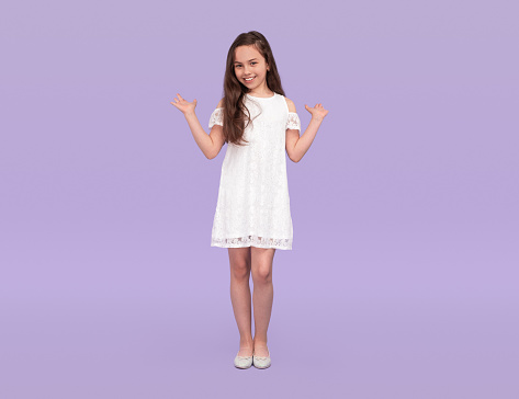 Full length teen girl in trendy white dress gesticulating and smiling for camera on sunny day ob violet background