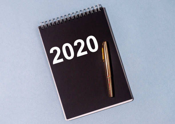 istock black Notebook with on blue violet background. Notebook or planner with text 2020 year with golden pen. 2020 summary recap review concept 1225629237