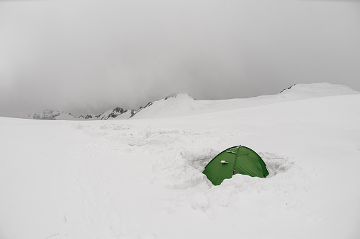Landscape of the green tent standing on the mountain hill covered by snow on the way on meteostation in Kazbek, Georgia