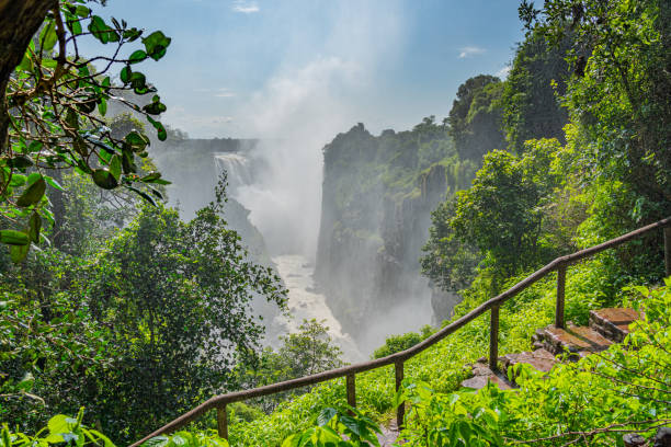 cataratas victoria en el río zambezi, frontera de zambia y zimbabue con cielo azul y un camino a pie - victoria falls waterfall zimbabwe zambia fotografías e imágenes de stock