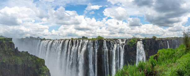 vista panorámica de las cataratas victoria del río zambezi, con cielo azul y nubes dramáticas - victoria falls waterfall zimbabwe zambia fotografías e imágenes de stock