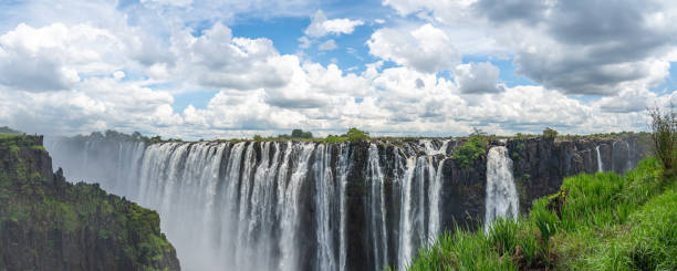 vue panoramique des chutes victoria de la rivière zambèze, avec le ciel bleu et les nuages dramatiques - victoria falls waterfall zimbabwe zambia photos et images de collection