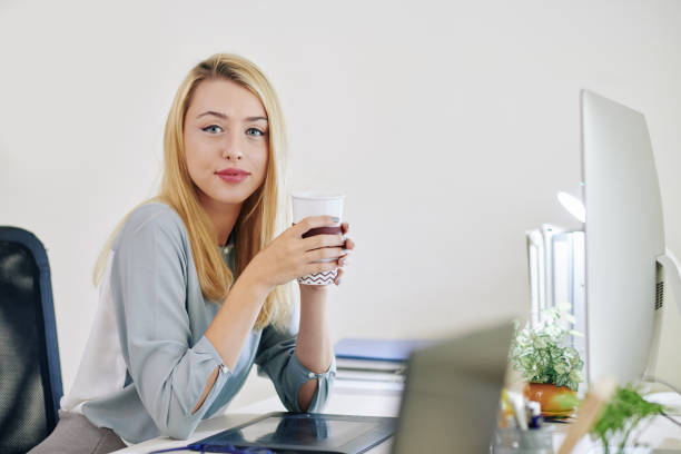 Portrait of young beautiful businesswoman drinking cup of take away coffee when sitting at her office desk