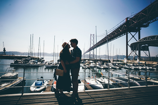 Romantic couplehugging in front of the bridge called April 25 in Lisbon and yachts port in Portugal at sunny summer day.