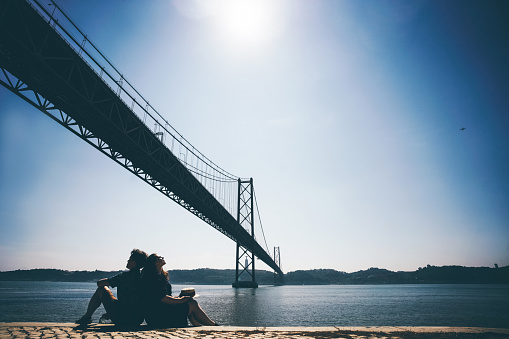 Romantic couple relaxing in front of the bridge called April 25 in Lisbon in Portugal at sunny summer day.