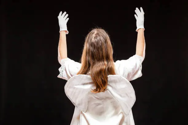 Portrait of male mime artist, isolated on black background. Back view of a man dressed like an angel standing with his hands risen. Symbol of invoke, plead, pray.