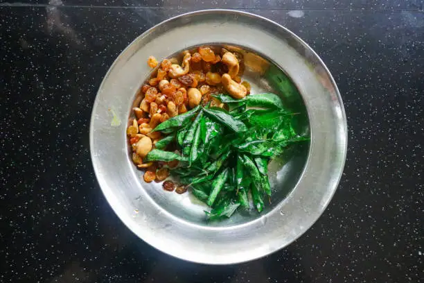 Cashew-nuts , raisins and curry leaves in a steel plate for coocking .