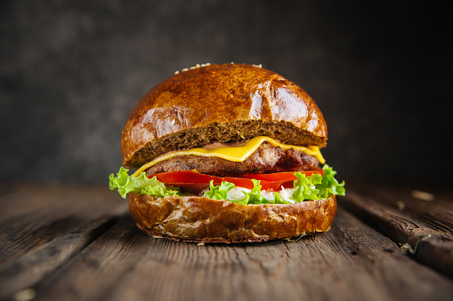 Side view closeup of a burger with a rye dark bun on the wooden table dark background, horizontal