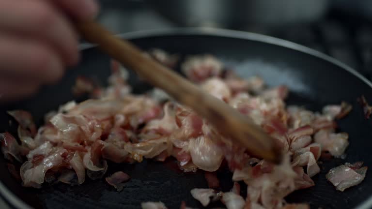 Mixing with a wooden spoon fresh juicy nicely chopped pancetta/bacon in a pan on the gas stove