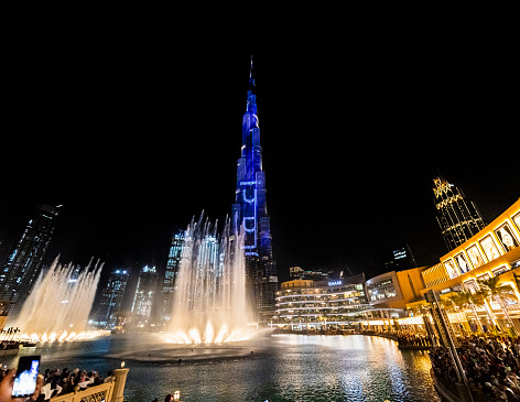 Dubai Fountain and the Burj Khalifa, the world tallest building, at night. Many people watching the show.