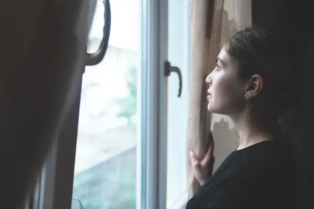 Photo of Woman back opening curtains and looking from window during COVID-19 pandemic