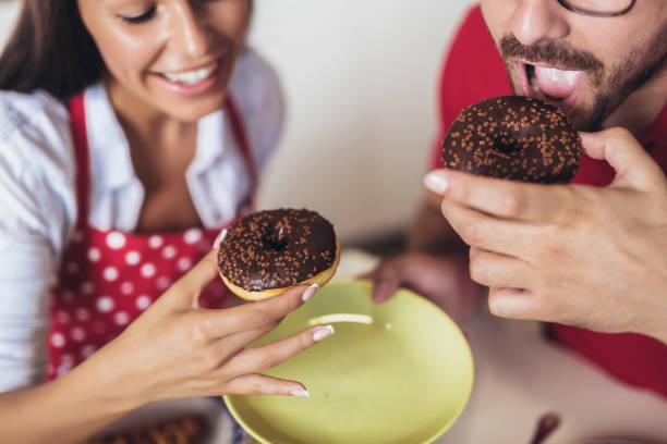istock Cheerful young couple having breakfast in kitchen eating donuts. 1225649318