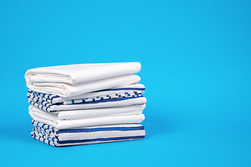 Towels and bed linen with storage solution for wardrobe at home. Pillowcases and sheets neatly stacked on blue background, front view, copy space for lettering
