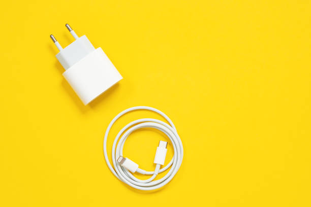 envuelto en un cable relámpago usb de anillo y adaptador de corriente para cargar teléfonos inteligentes y dispositivos o para conectar aparatos a un ordenador o portátil en fondo amarillo, vista superior, espacio de copia - expendable fotografías e imágenes de stock