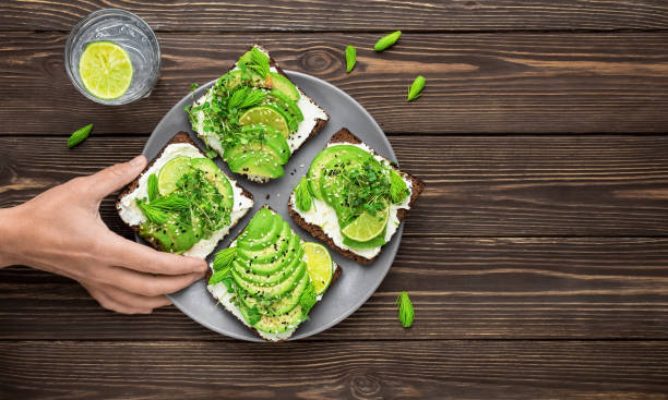 la mano de la mujer toma sándwich del plato. sandwich sobre pan de centeno con aguacate, queso, micro-verdes. snack vegetariano saludable, plano con espacio de copia - avocado seed cross section food and drink fotografías e imágenes de stock