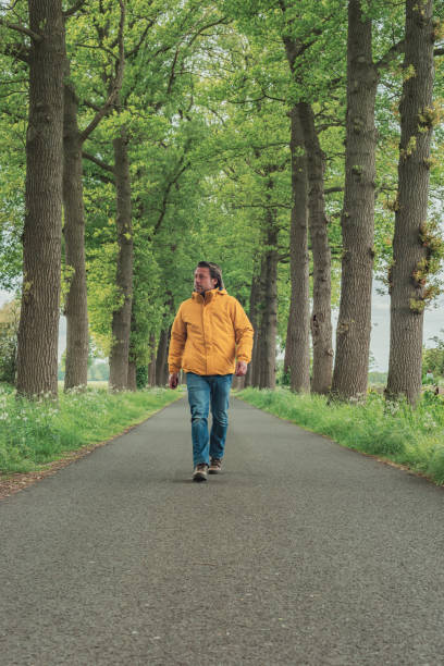 istock Man in yellow jacket and jeans walks on country road in springtime. 1225656721