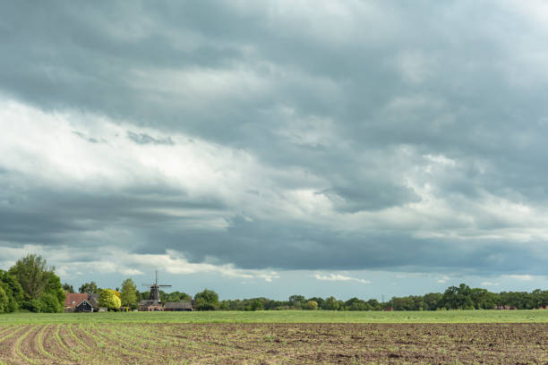 istock Farmland with trees and windmill on the horizon under cloudy sky. 1225656753