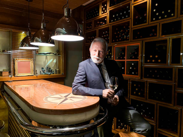 고급스러운 와인 옷장에서 스파클링 와인을 즐기는 수석 우아한 남자 - winetasting wine wine rack bar counter 뉴스 사진 이미지