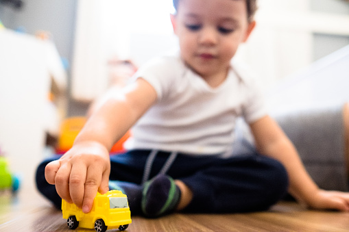 Toddler boy playing with a yellow truck at the bedroom floor