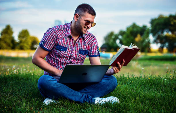 istock Student searching informations with laptop and reading a book in the university park. Education, lifestyle concept 1225669520