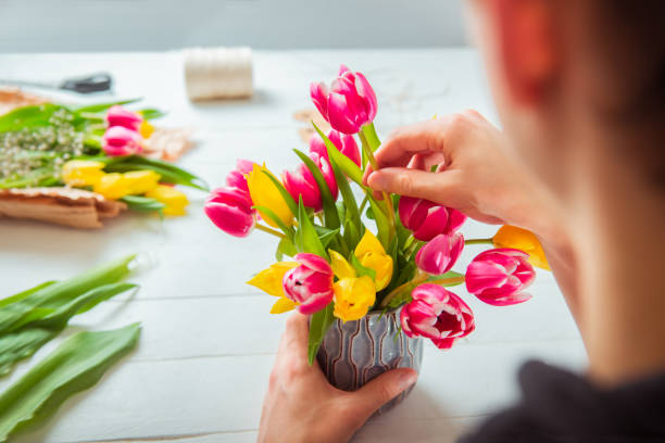 チューリップを使って春の花束を作る若い男はいない。植物学のオンライン自己教育。フラワーアレンジを学ぶ。花の配達。男性の花屋は注文を作成します。選択的フォーカス。 - flower arranging ストックフォトと画像