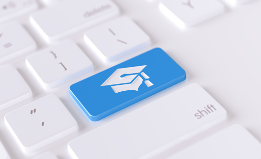 Graduation cap icon written on a blue button of a computer keyboard. Horizontal composition with selective focus and copy space. High angle view.  Online education concept.