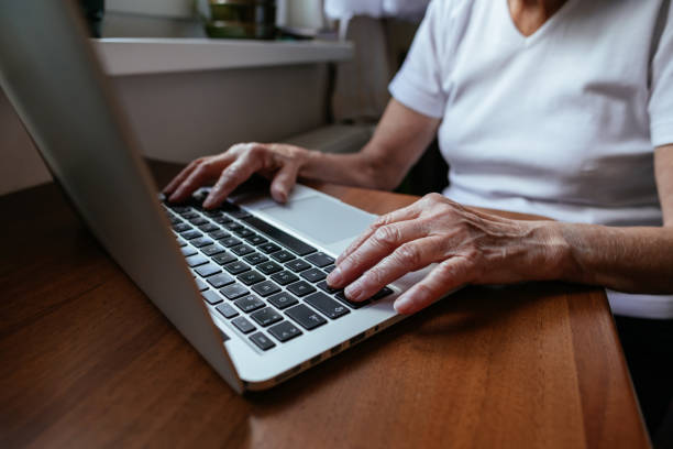 Close up of elderly woman hands typing on notebook. stock photo