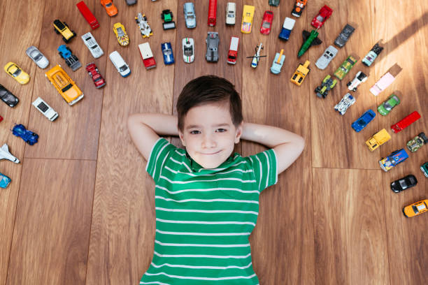 Cute 5 year old boy lying on wooden floor surrounded with car toys. stock photo