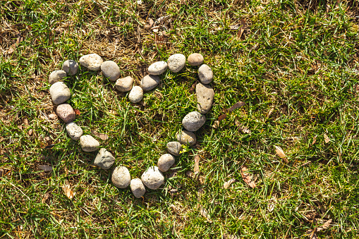 Over head shot of rocks shaped as a love heart laid out on green grass.