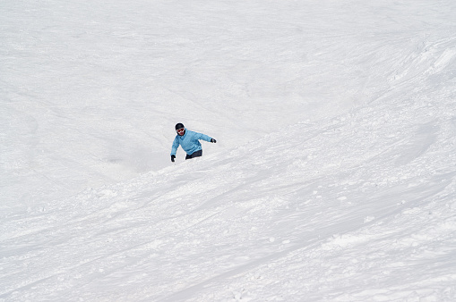 Snowboarder before jump on snowy ski slope at high winter mountains in sunny cold day