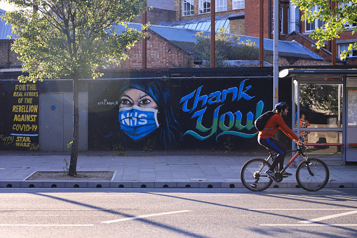 London, England - May 05, 2020. Member of the public on a daily cycling routine. Art featuring gratitude to NHS on the fence, Elephant & Castle, London.