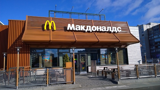 Pskov, Russia - March 9, 2020: McDonald's fast food store in the  city center. Brown colour facade of the McCafe. No people near the building. McDelivery service. Contact-free Payment. Franchisees