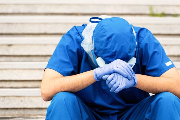 Serious, overworked, very sad male health care worker Young serious overworked, male mature health care worker sitting looking down very sad state of emergency stock pictures, royalty-free photos & images