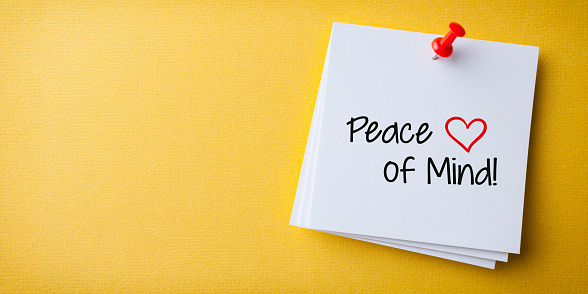 White Sticky Note With Peace of Mind And Red Push Pin On Yellow Background